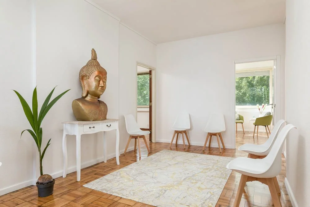 Sala com cadeiras brancas, um tapete claro e uma escultura de Buda dourada na parede.