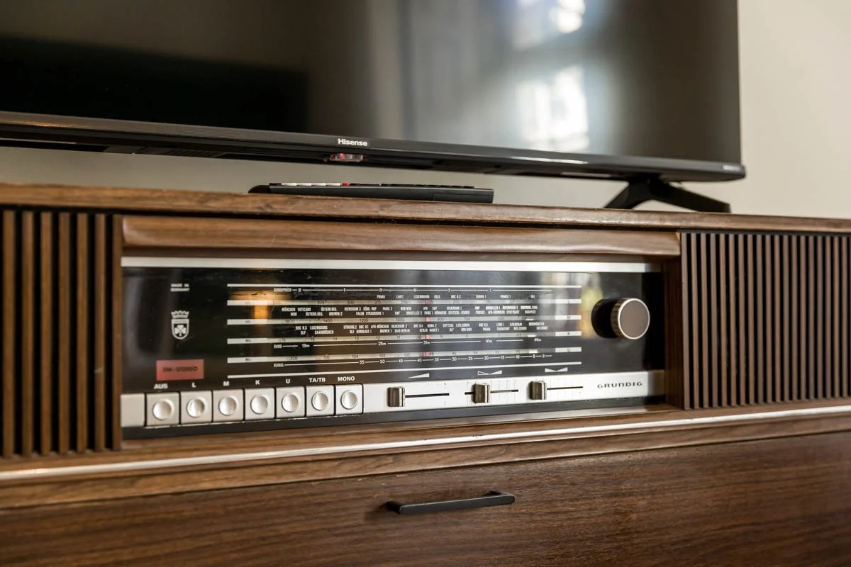 Rádio vintage com acabamento de madeira, controle de volume e botões para sintonizar estações, colocado em móvel de madeira.