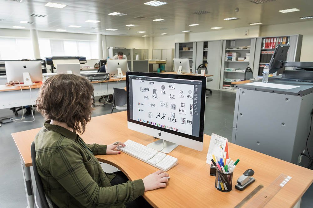 Pessoa trabalhando em um escritório com vários computadores Apple disponíveis.