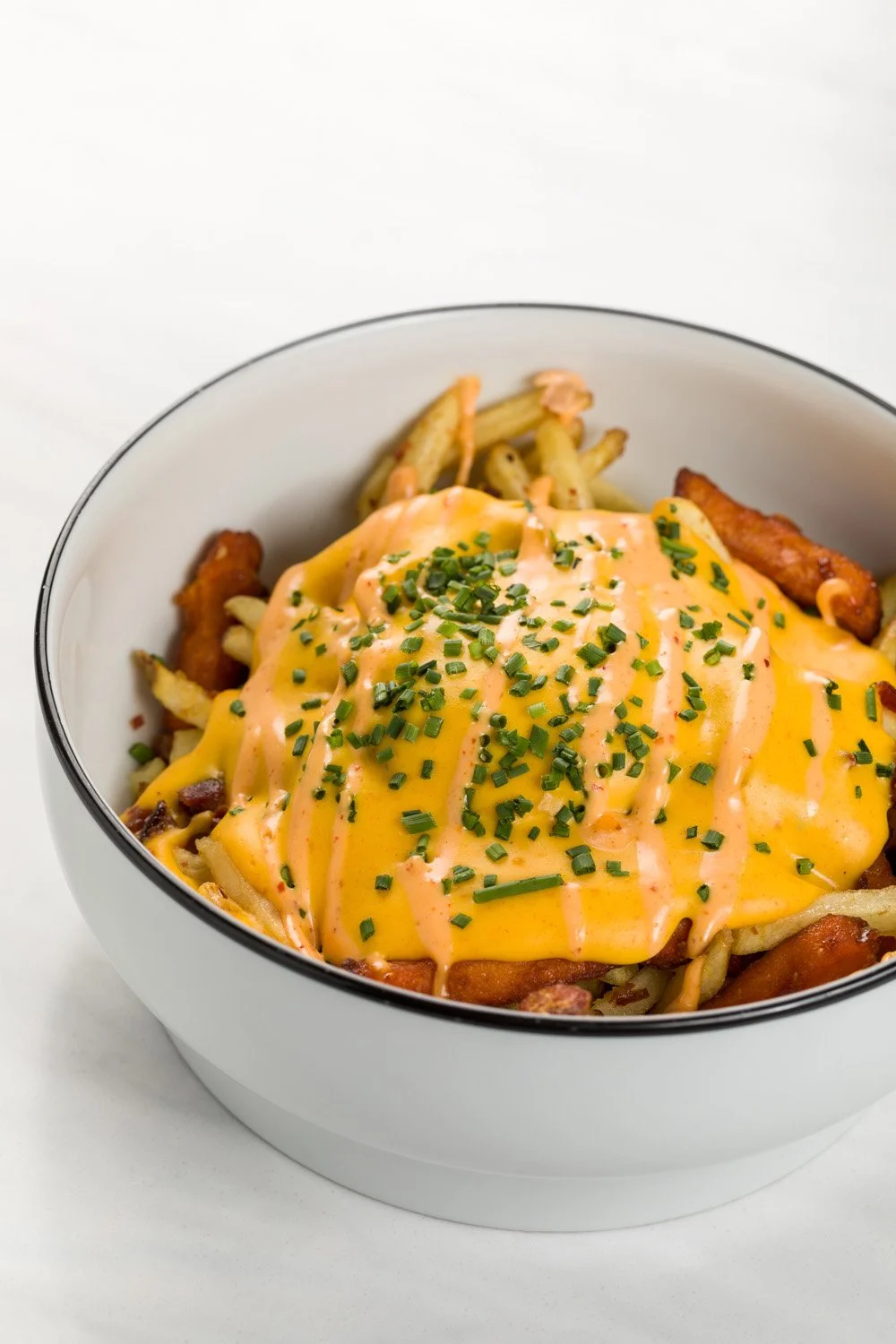 Prato com batatas fritas, queijo derretido, molho e cebolinha
