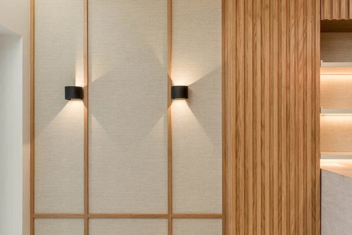 Parede de parede com duas luminárias de maneira simétrica, em um ambiente com decoração em tons de marrom claro e madeira.