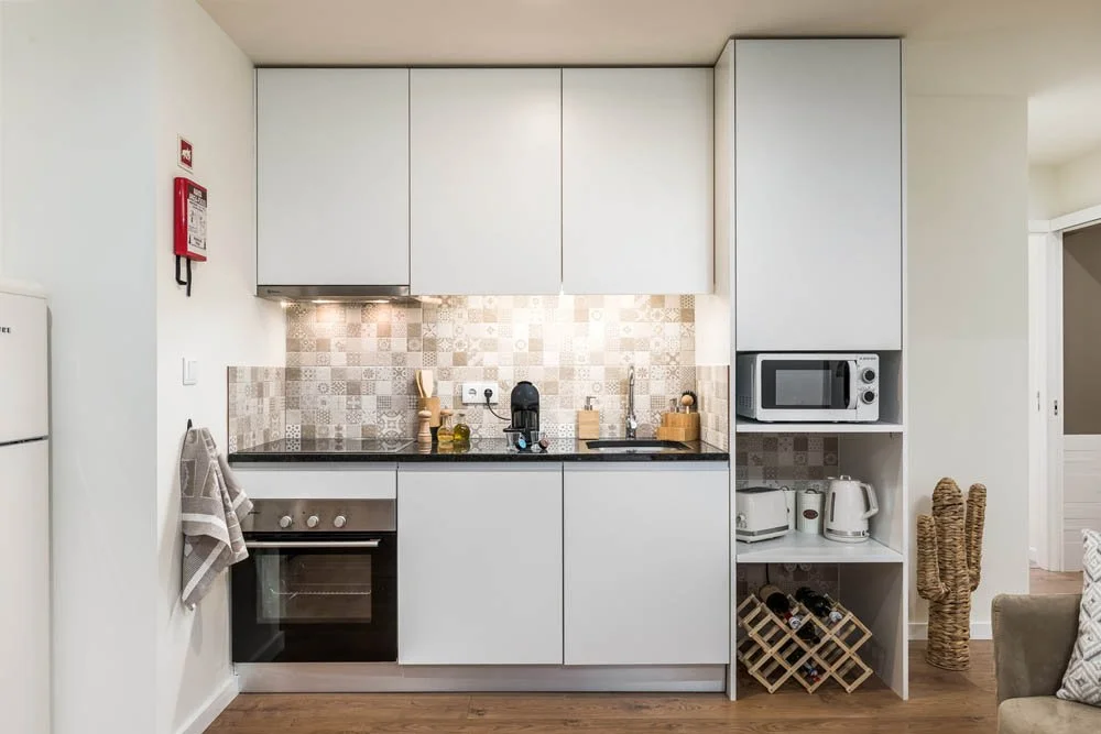 Cozinha moderna com armários brancos, backsplash com azulejos decorativos, eletrodomésticos como micro-ondas, geladeira, forno, e utensílios como liquidificador e cafeteira.