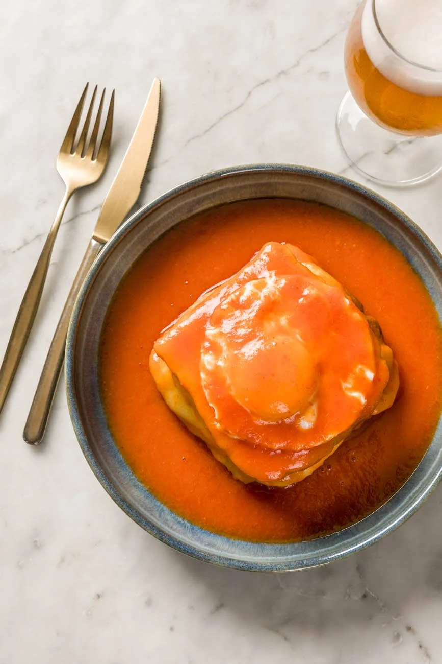 Prato com um pedaço de lasanha coberto com molho de tomate, acompanhado de um copo de cerveja ao lado.