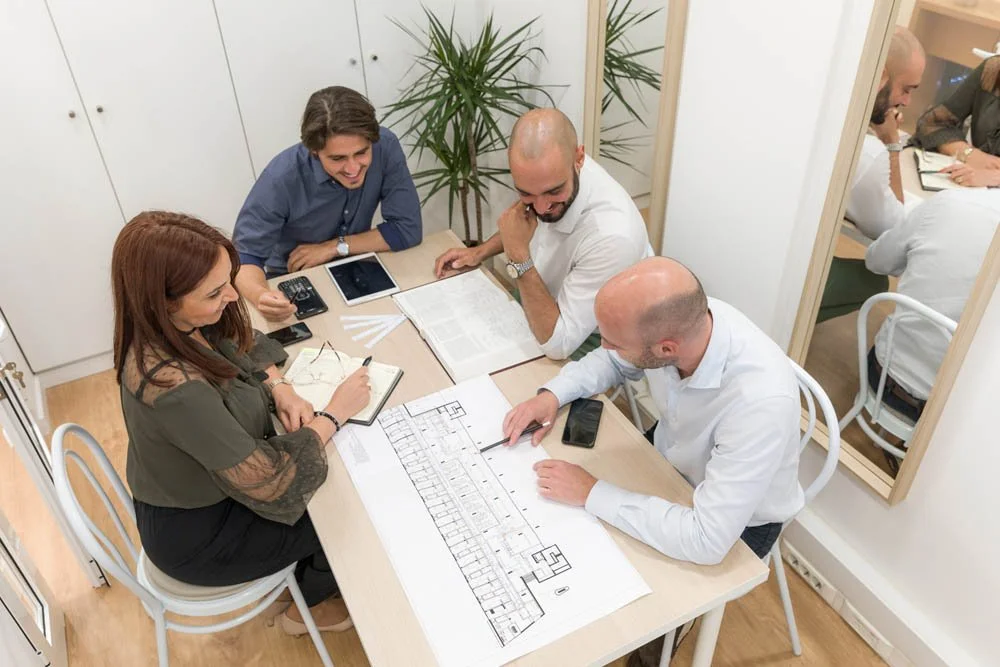 Quatro pessoas em uma reunião de trabalho, discutindo um projeto arquitetônico ou de construção, em um ambiente de escritório.