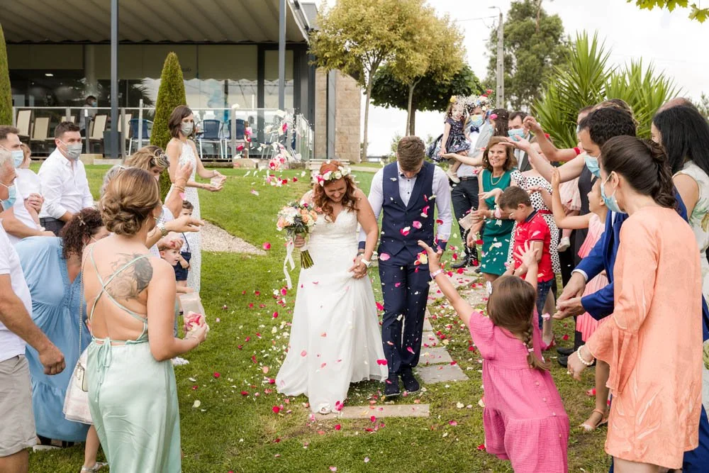 Casal de noivos caminhando por um caminho de pedras enquanto seus convidados jogam pétalas de rosa em volta na celebração de casamento ao ar livre.