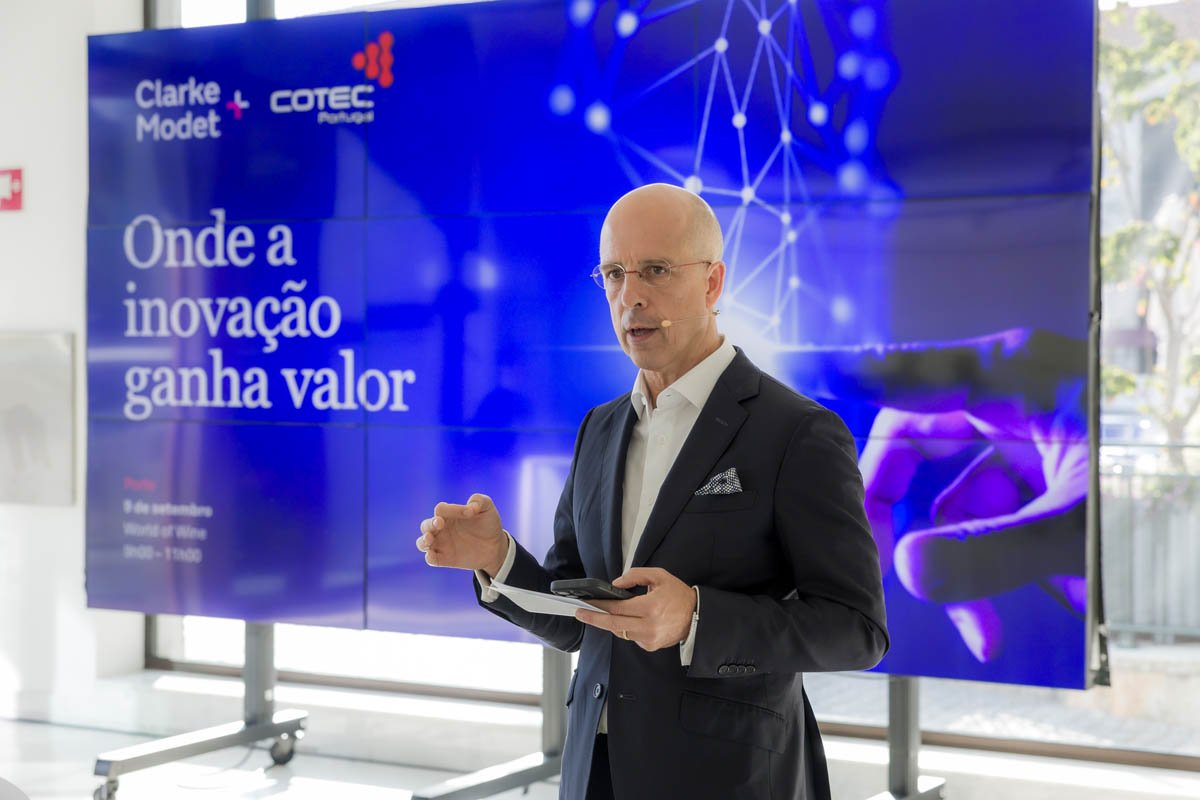 Homem de terno apresentando em frente a uma tela com texto em português, que diz "Onde a inovação ganha valor", em um evento da Clarke Model+ e Cotec Portugal.