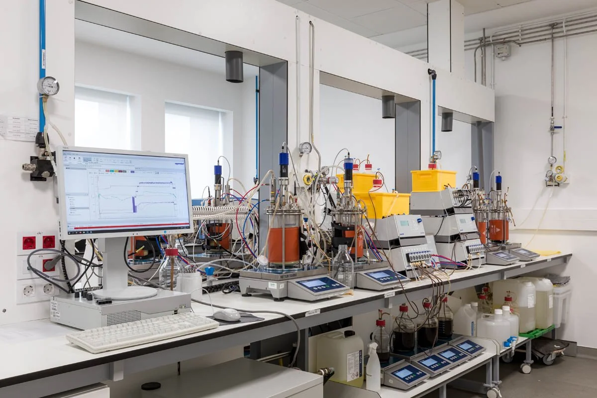 Laboratório com equipamentos científicos, incluindo computadores, tubos de ensaio, líquidos e instrumentos de medição, utilizados para experimentos e análises laboratoriais.