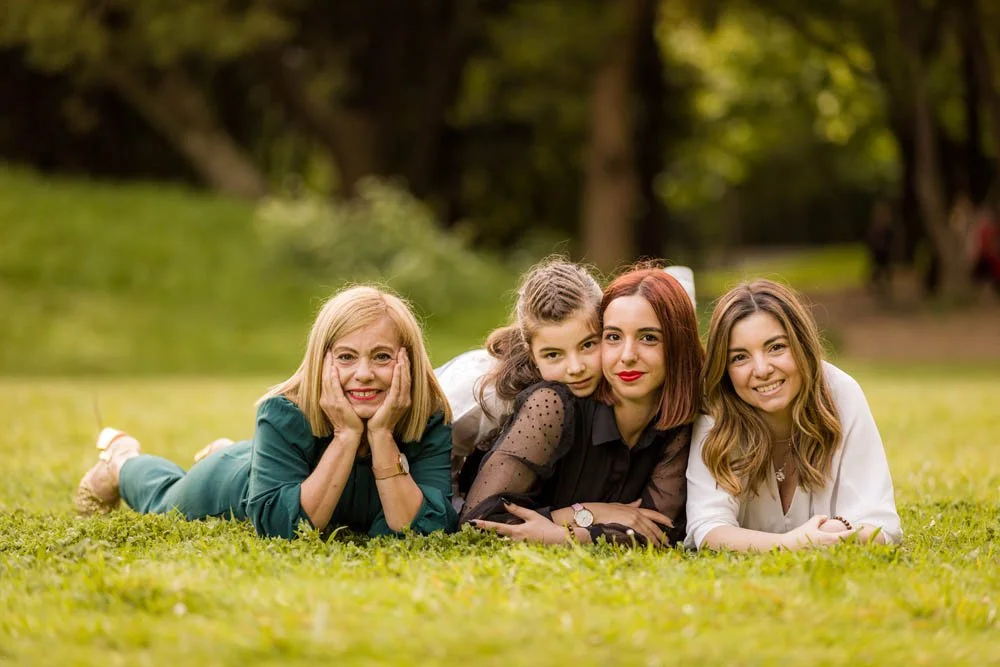 Quatro mulheres de diferentes idades, mães e filhas, deitados em um gramado verde em um parque, sorrindo para a câmera.