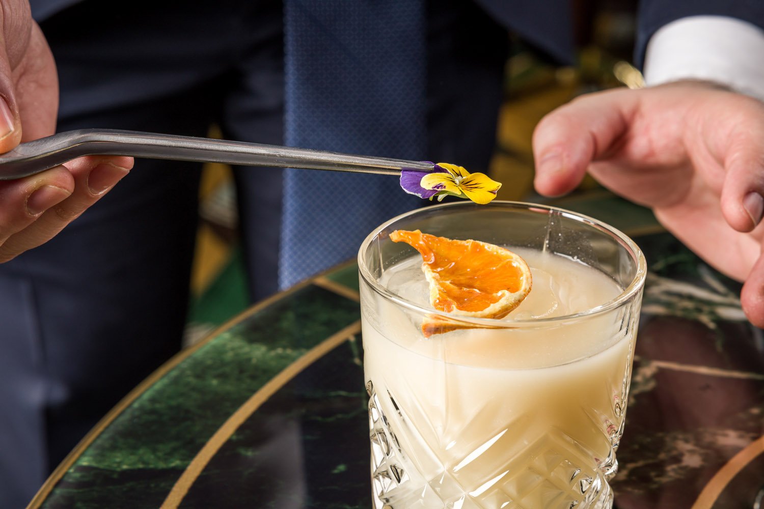 Pessoa decorando um cóctel com uma flor e uma fatia de laranja na bebida.