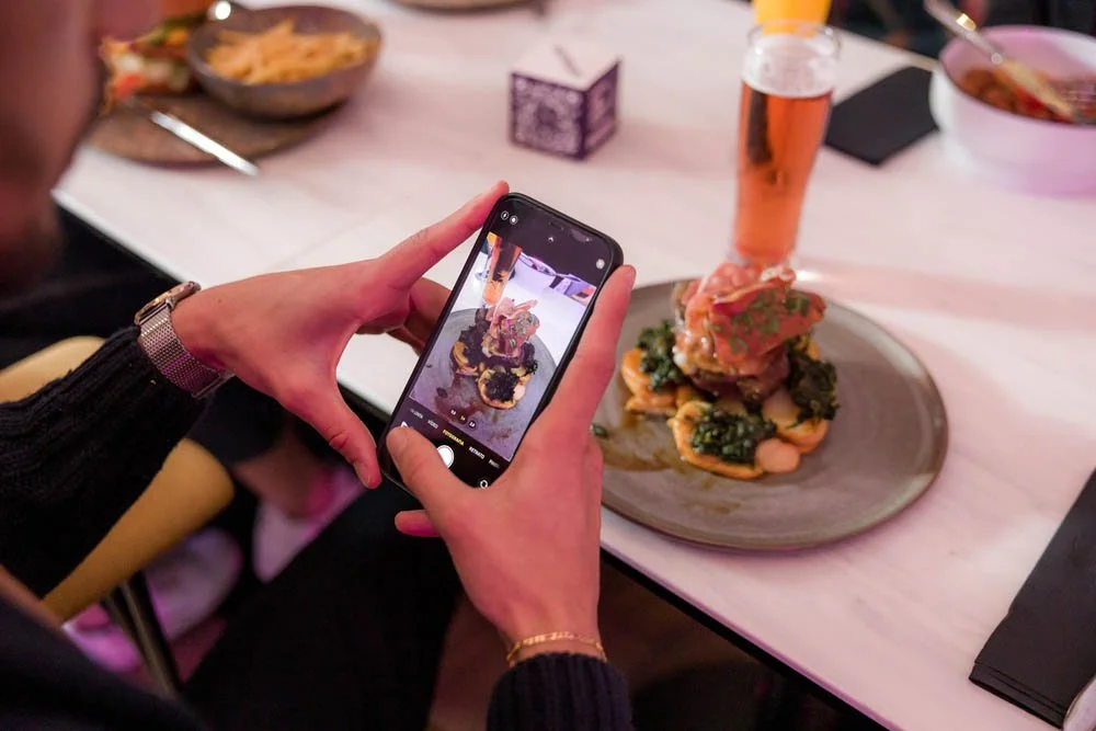 Pessoa tirando uma foto de um prato de comida em um restaurante.