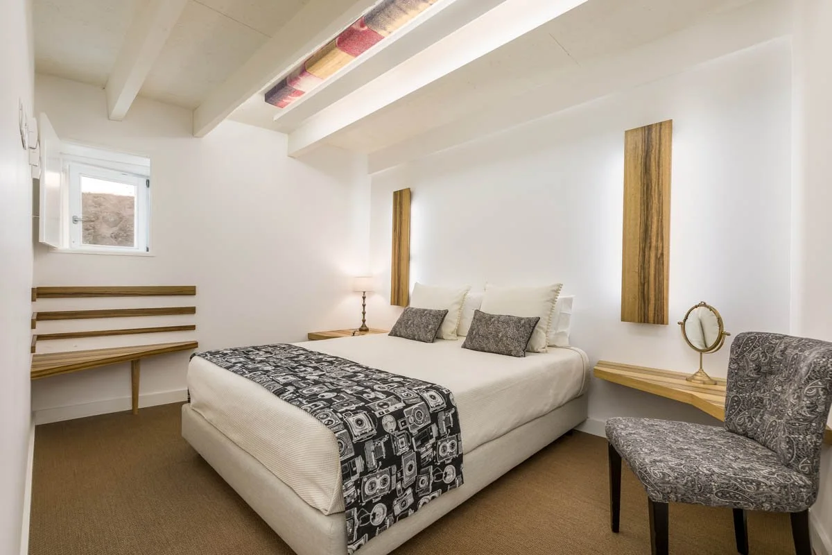 Quarto decorado com cama, almofadas, abajur, espelho, poltrona e parede com detalhes em madeira