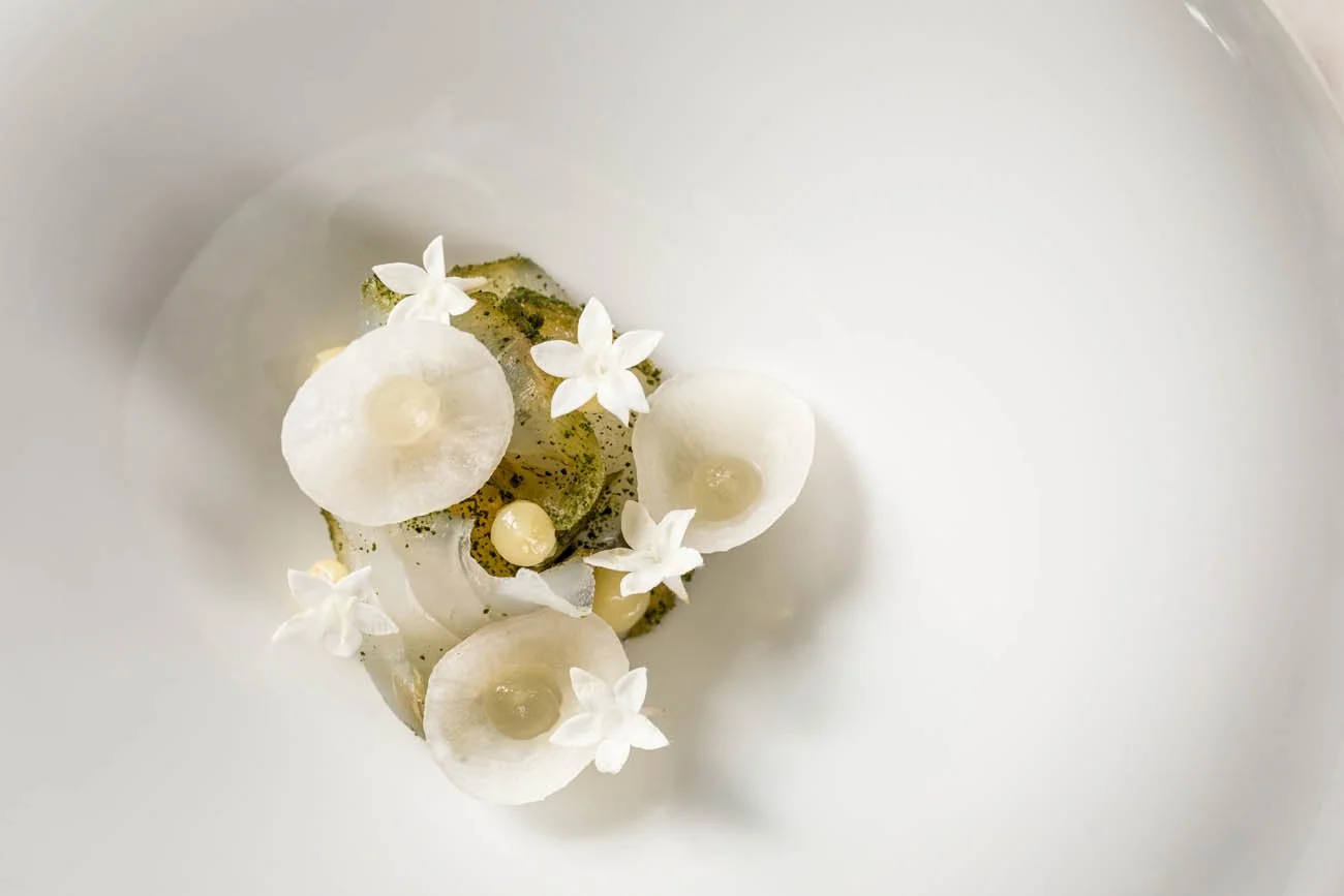 Prato de comida sofisticada com flores brancas e ingredientes delicados em uma apresentação minimalista.