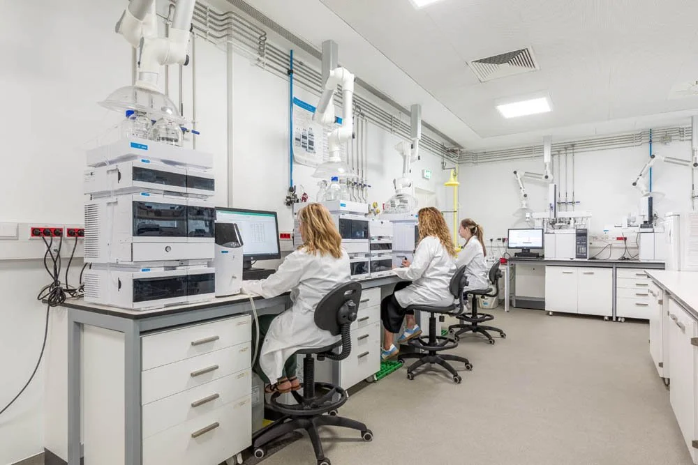 Laboratório com três cientistas usando computadores e equipamentos de laboratório com exaustores no teto.