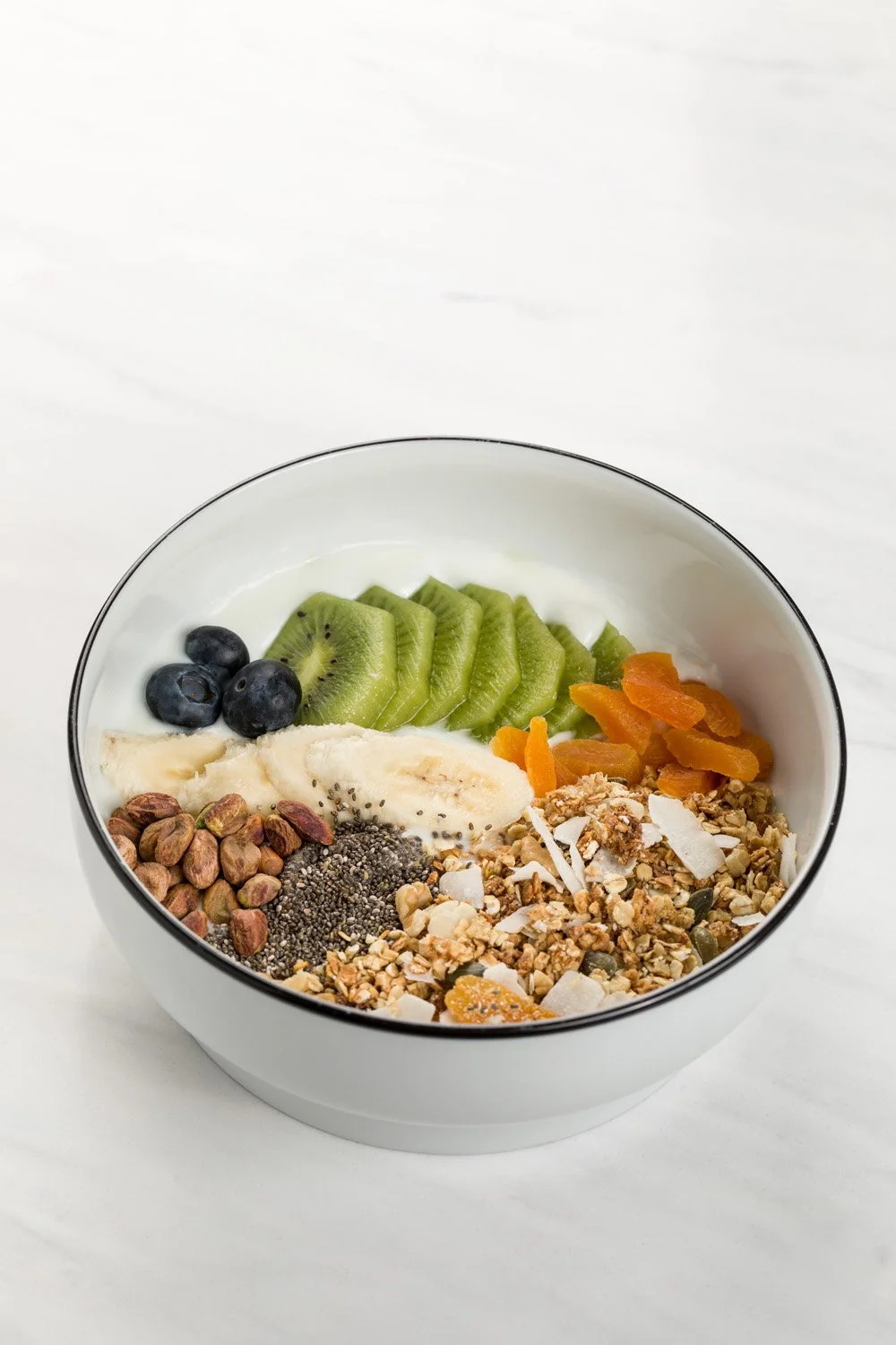 Tigela com frutas, sementes, aveia, granola e iogurte.