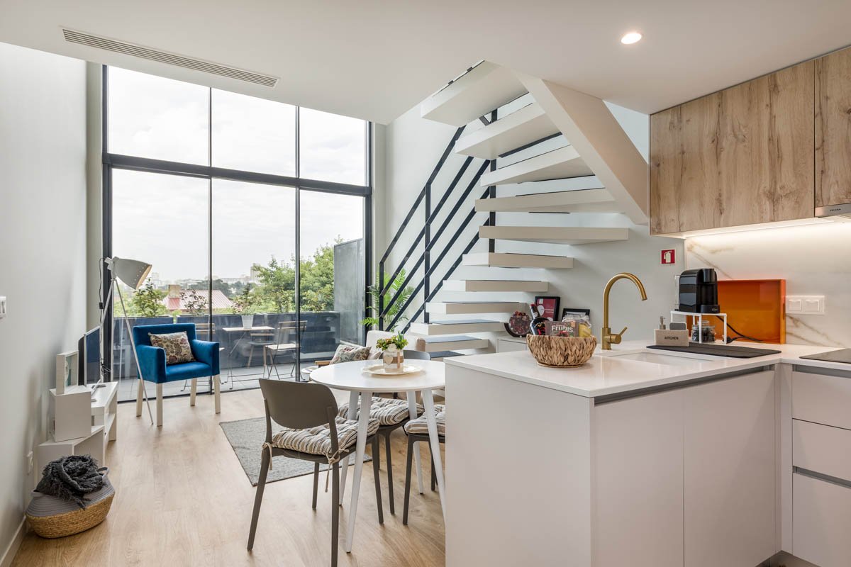 Interior de um apartamento moderno com sala de estar, área de jantar, cozinha e escada de viagem, com vista para um espaço externo com varanda.