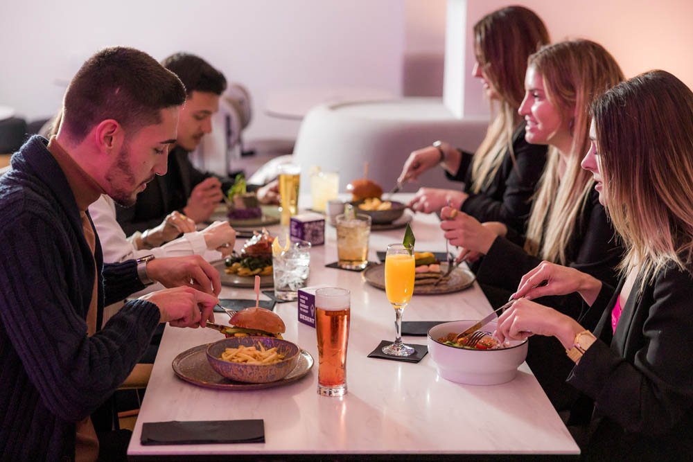 Pessoas jantando em um restaurante, com pratos de comida e bebidas na mesa.