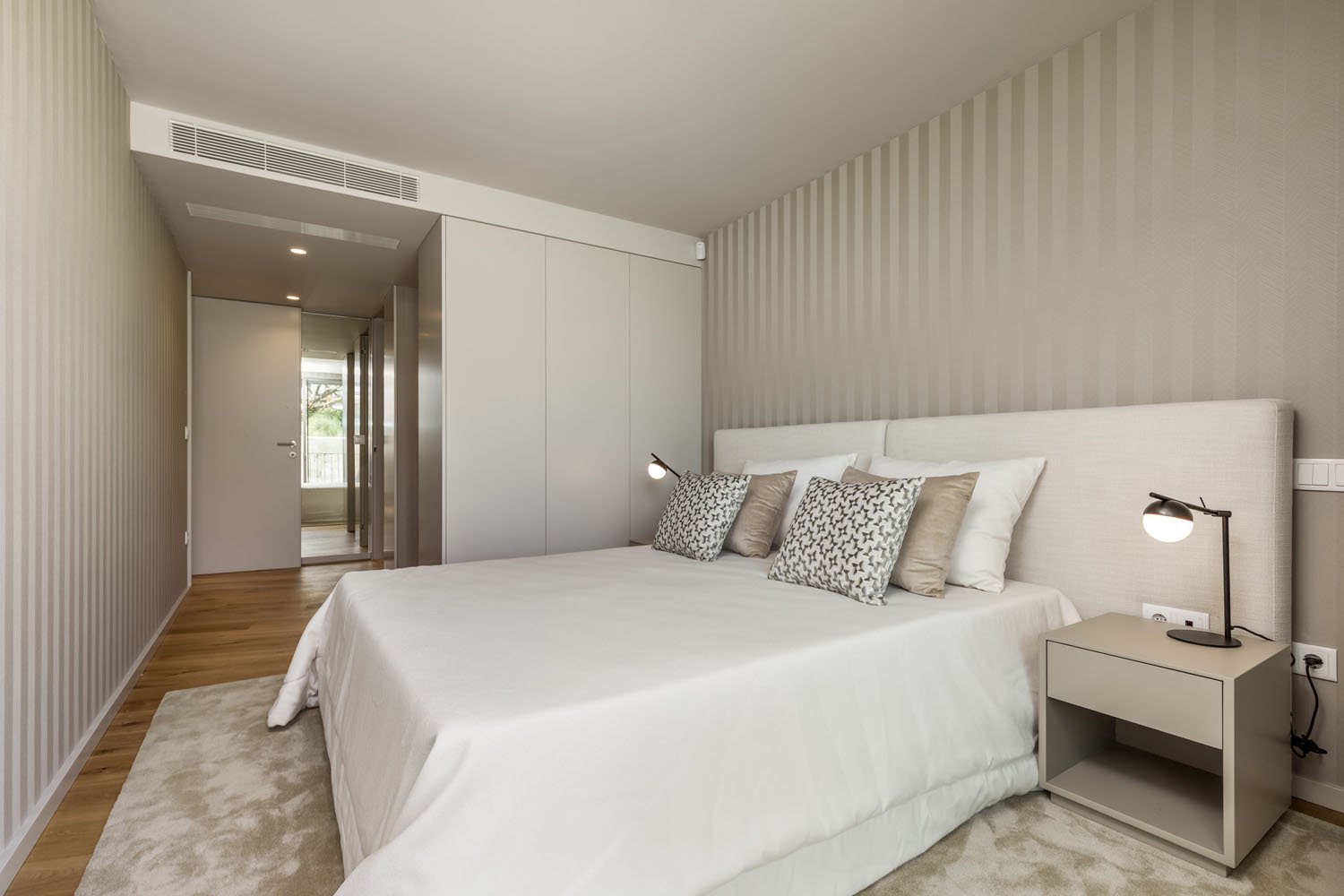Quarto com cama de cama branca, travesseiros decorativos cinza, paredes de tomadas de linhas verticais e iluminação suave