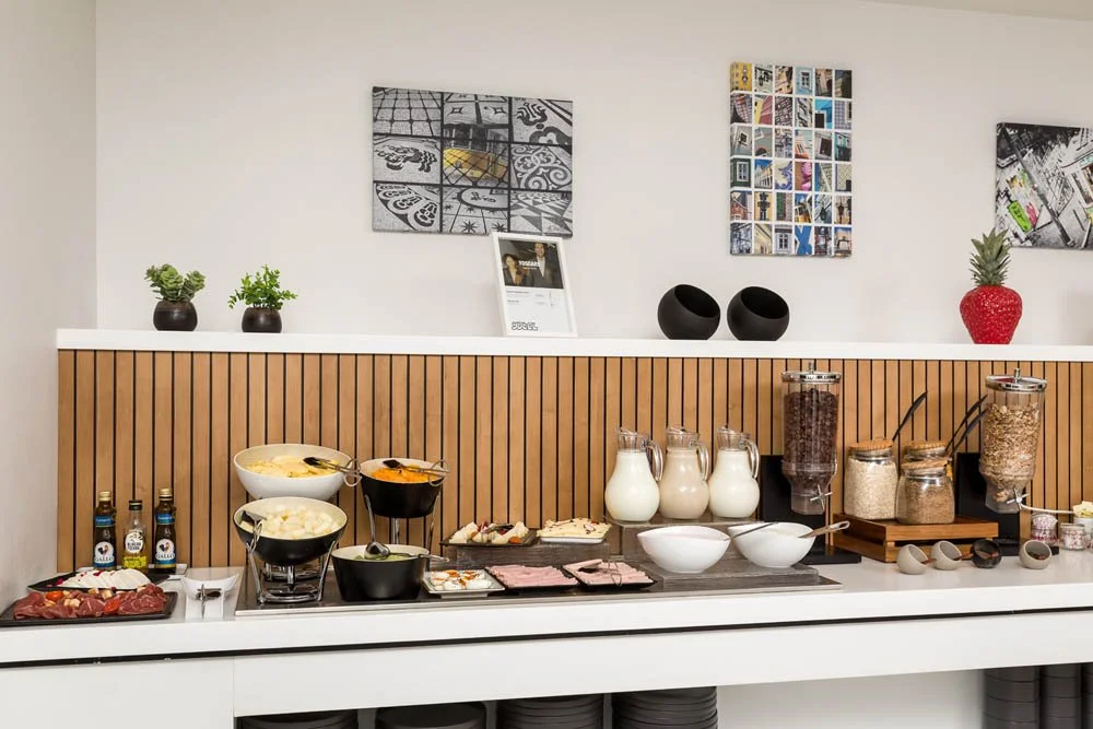Buffet de café da manhã com variedades de cereais, leite, frutas, e itens de café da manhã em uma bancada de restaurante.