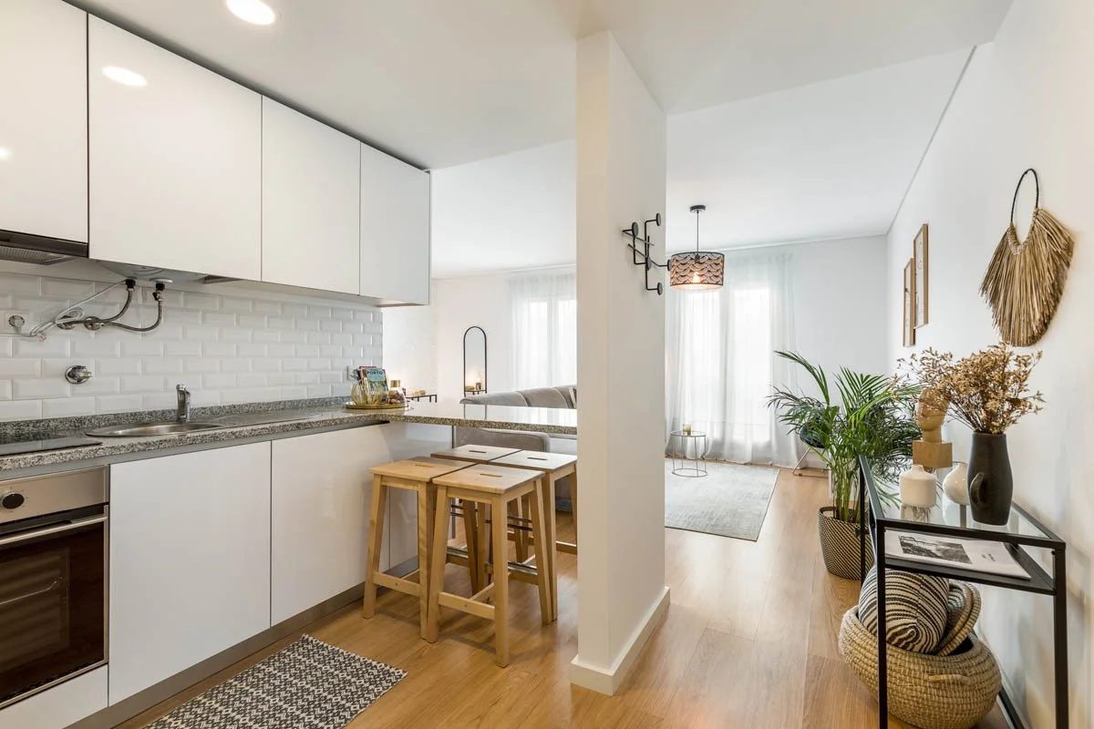 Imagem de um espaço aberto com cozinha e sala de estar decorada com plantas, quadros e móveis de estilo minimalista em tons neutros.