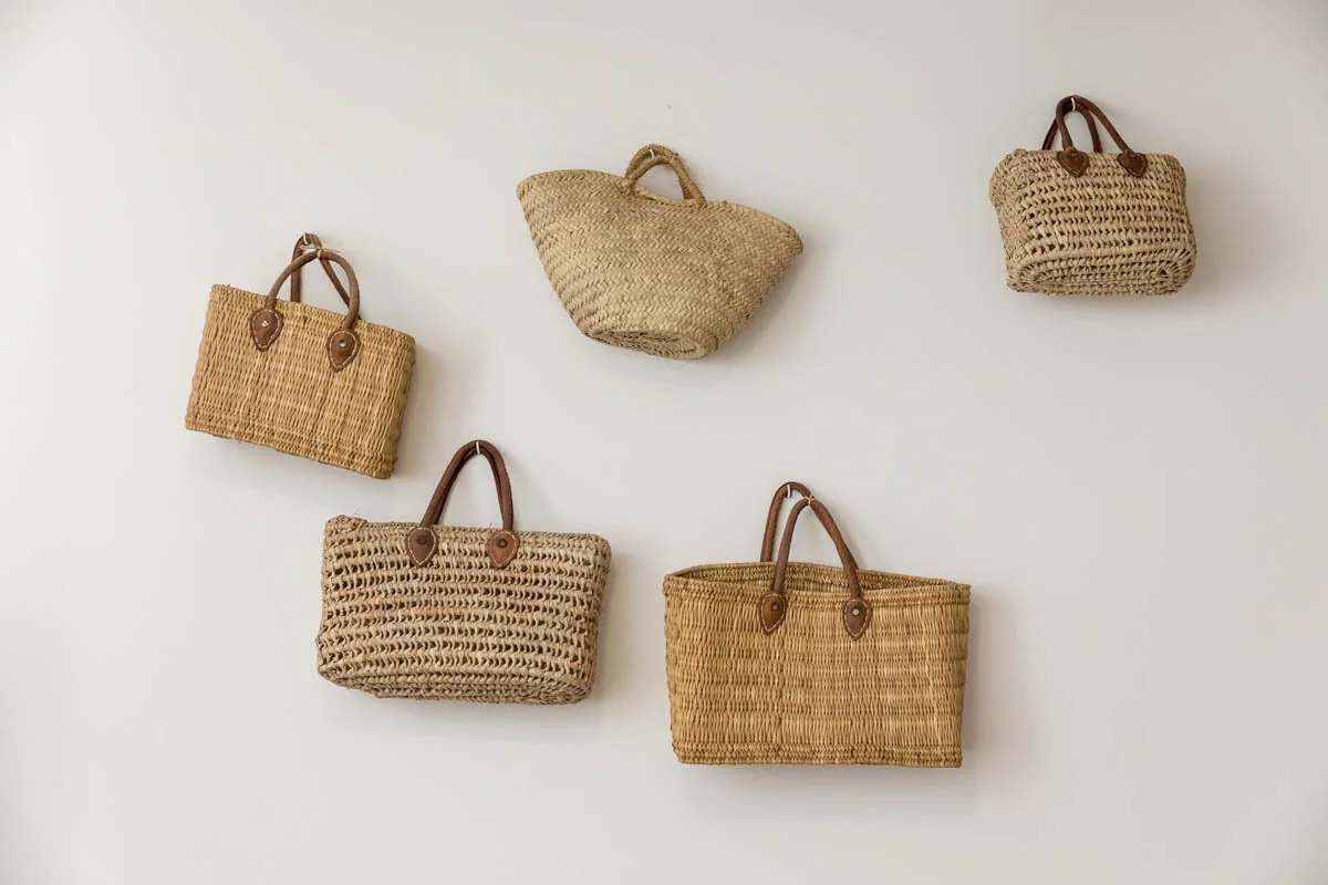 Seis bolsas de palha e fibra natural penduradas na parede branca