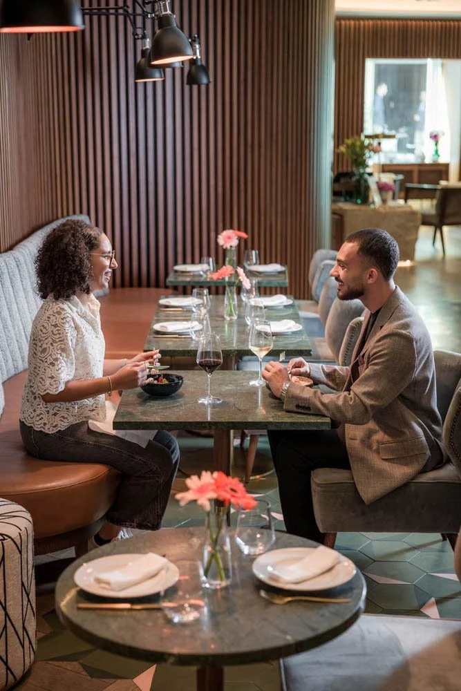 Homens e uma mulher conversando em um restaurante, com taças de vinho na mesa