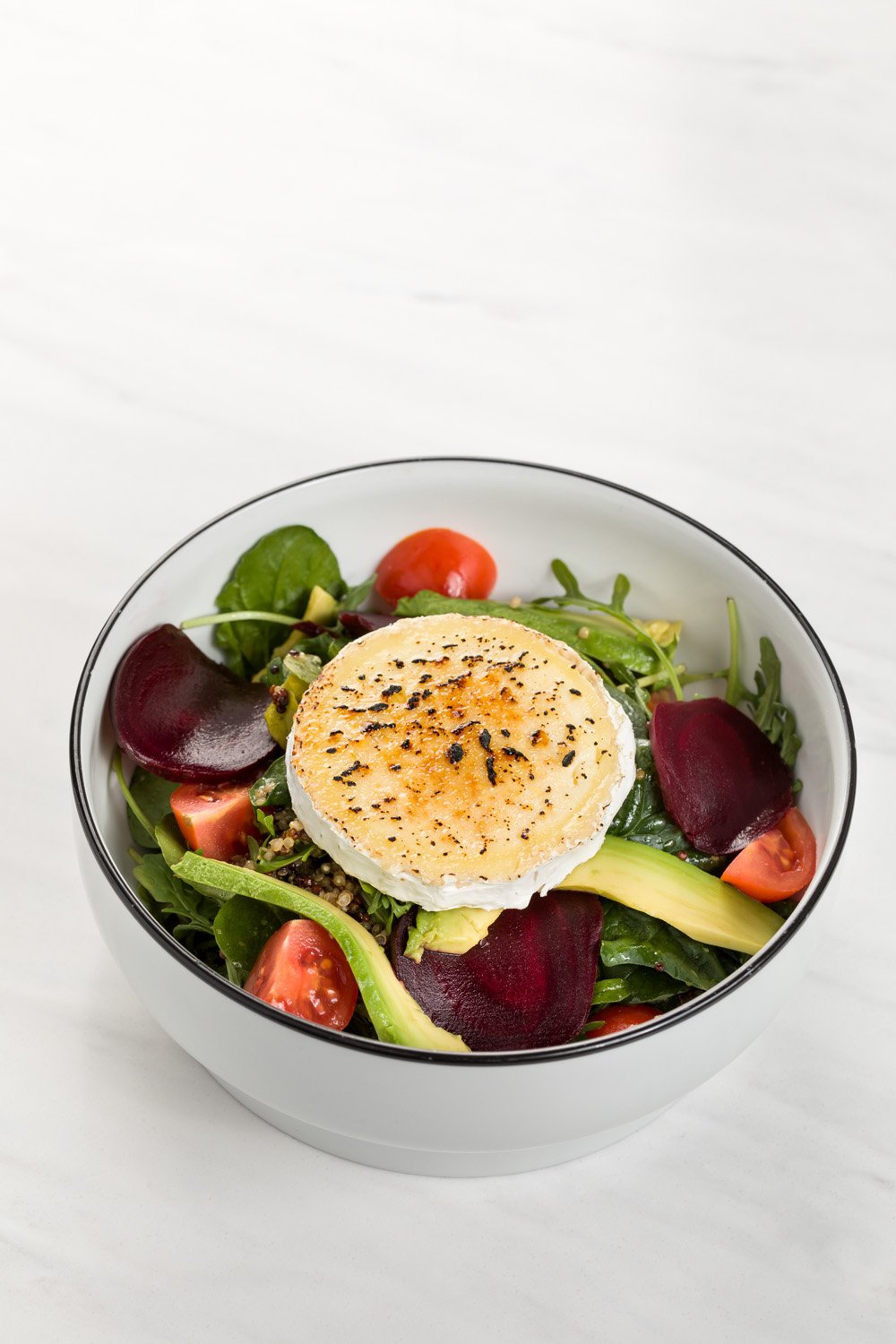 Salada com folhas verdes, tomates cereja, beterraba, abacate, e um ovo poché por cima.