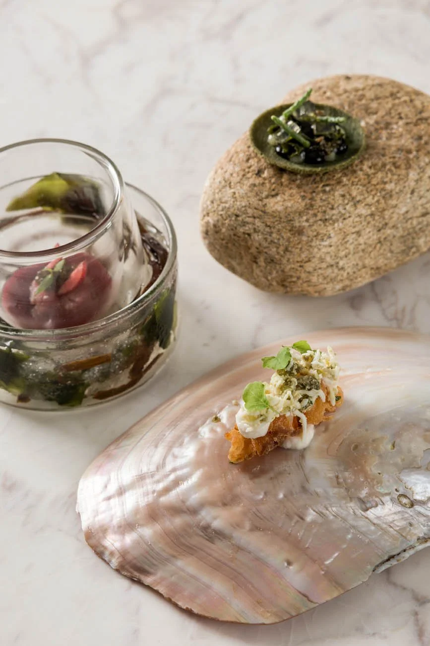 Aclaração de uma pedra com uma pequena tigela de molho de verde, uma concha com marisco e uma camada de areia.