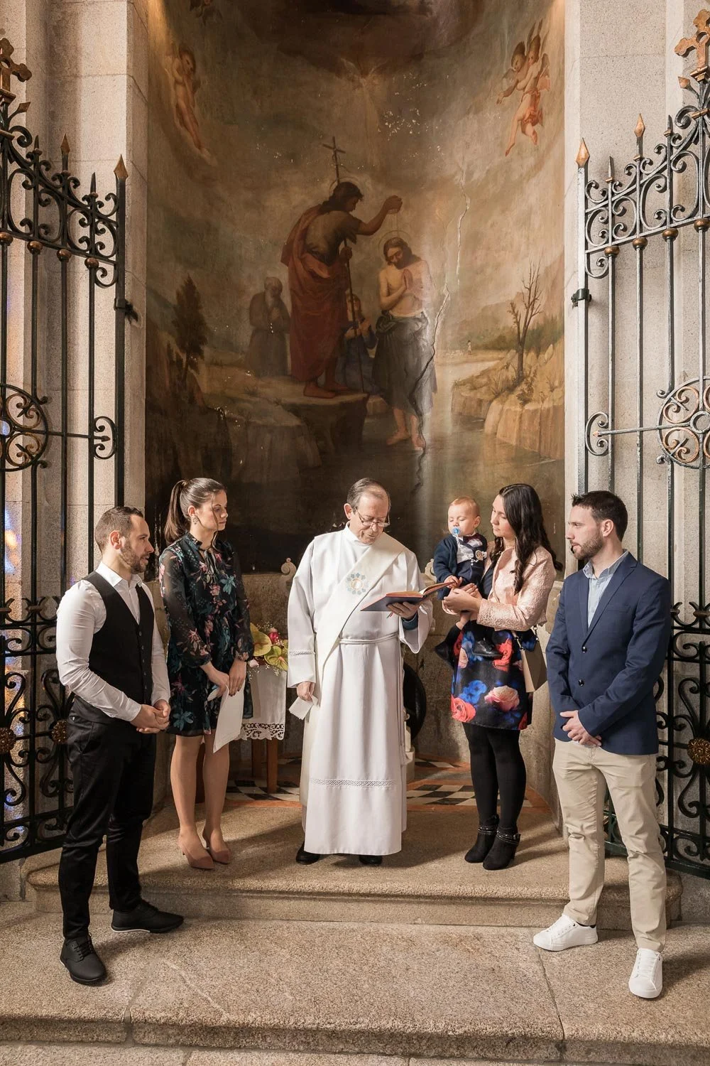 Grupo de pessoas participando de cerimônia religiosa diante de uma grande pintura de Jesus batizando um homem, dentro de uma igreja.
