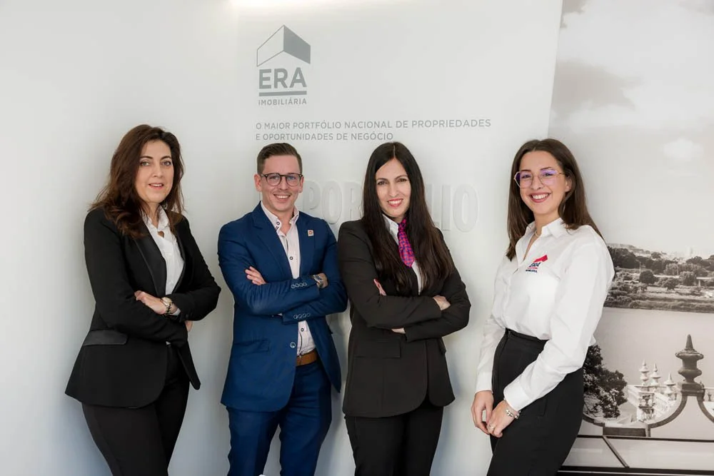 quatro pessoas de terno posando para foto em ambiente corporativo com marca ERA Imobiliária ao fundo