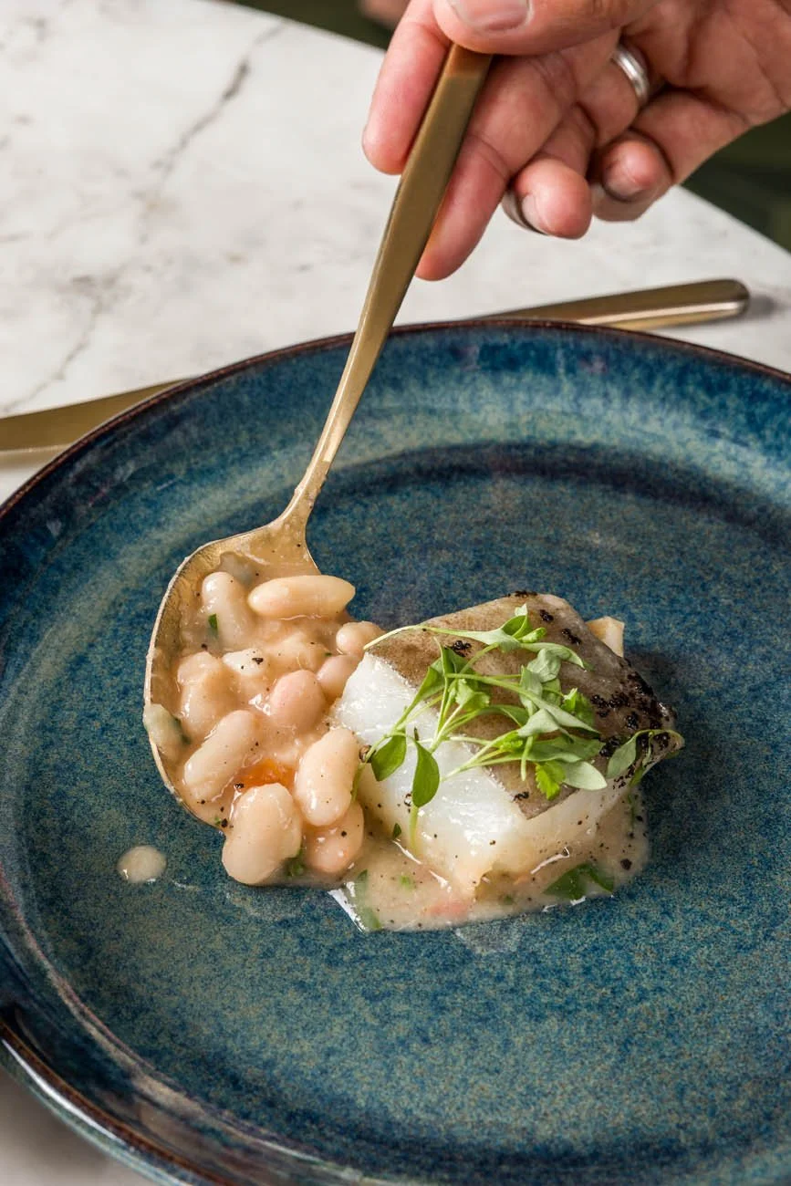 Prato com peixe, feijão branco e microverdes em uma tigela azul escura.