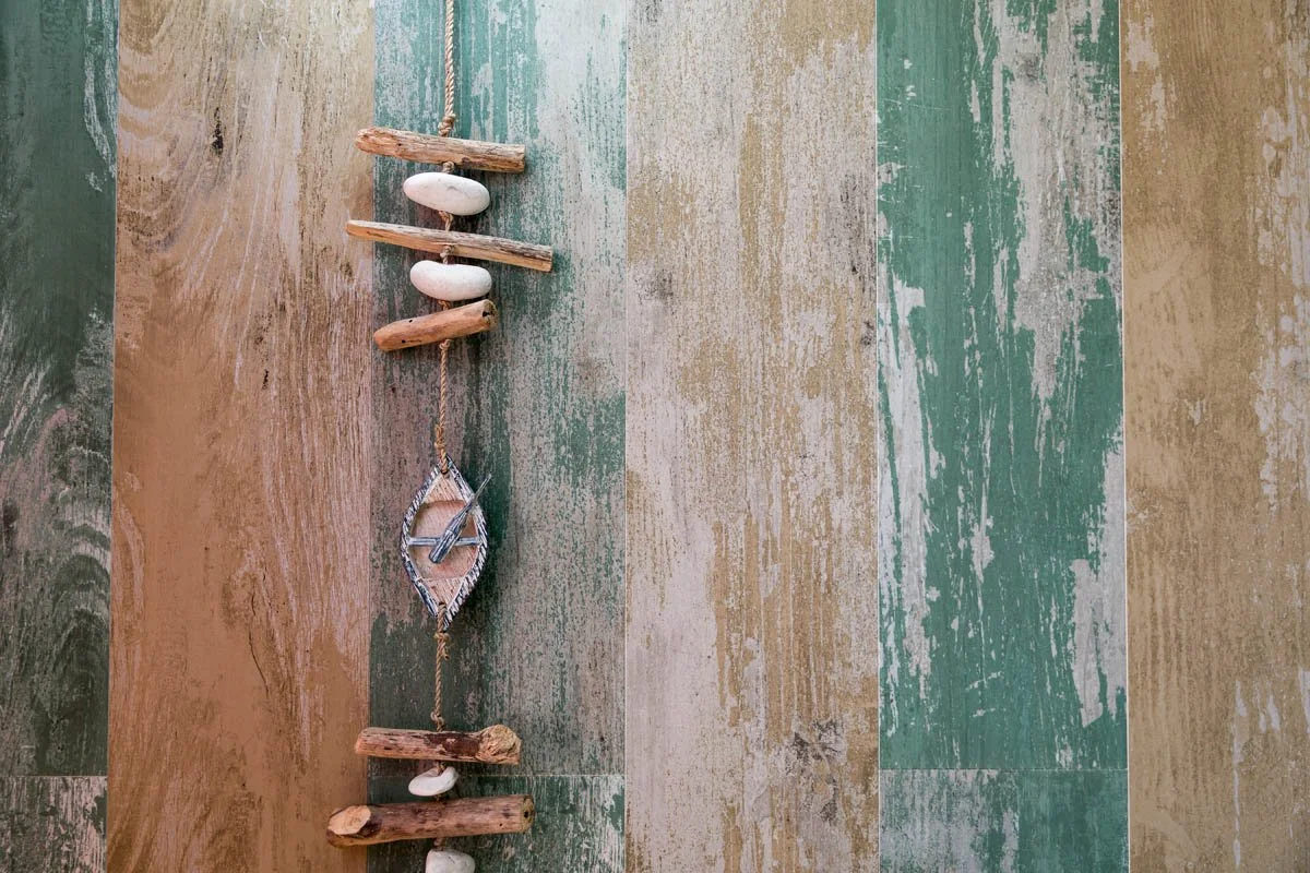 Decoração de parede com tábuas de madeira, pedras brancas e uma corda com um símbolo de play, formando uma peça decorativa marítima.