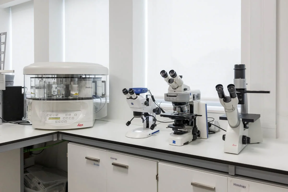 Equipamentos de laboratório, incluindo um autoclave e três microscópios, em uma bancada de pesquisa.