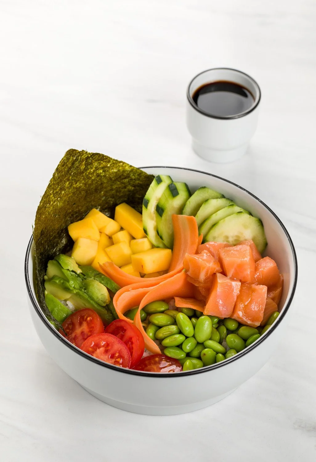 Salada de ingredientes frescos como tomate, abacate, pepino, ao lado de um copo de café preto em uma tigela branca