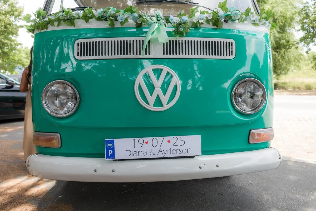 Furgão Volkswagen decorado com flores e fita de casamento, com uma placa exibindo a data 19/07/25 e os nomes Diana & Ayrleton.