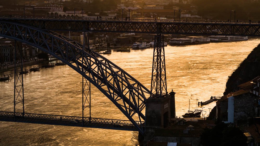 Ponte Thames em Londres durante o pôr do sol, com o rio Tâmisa ao fundo e barcos na água, vista de uma ponte de ferro.