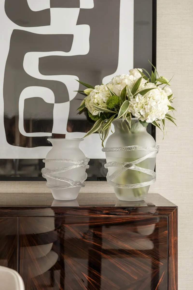 Vasos e arranjo de flores brancas em uma mesa de madeira polida na parede com um quadro decorativo ao fundo.