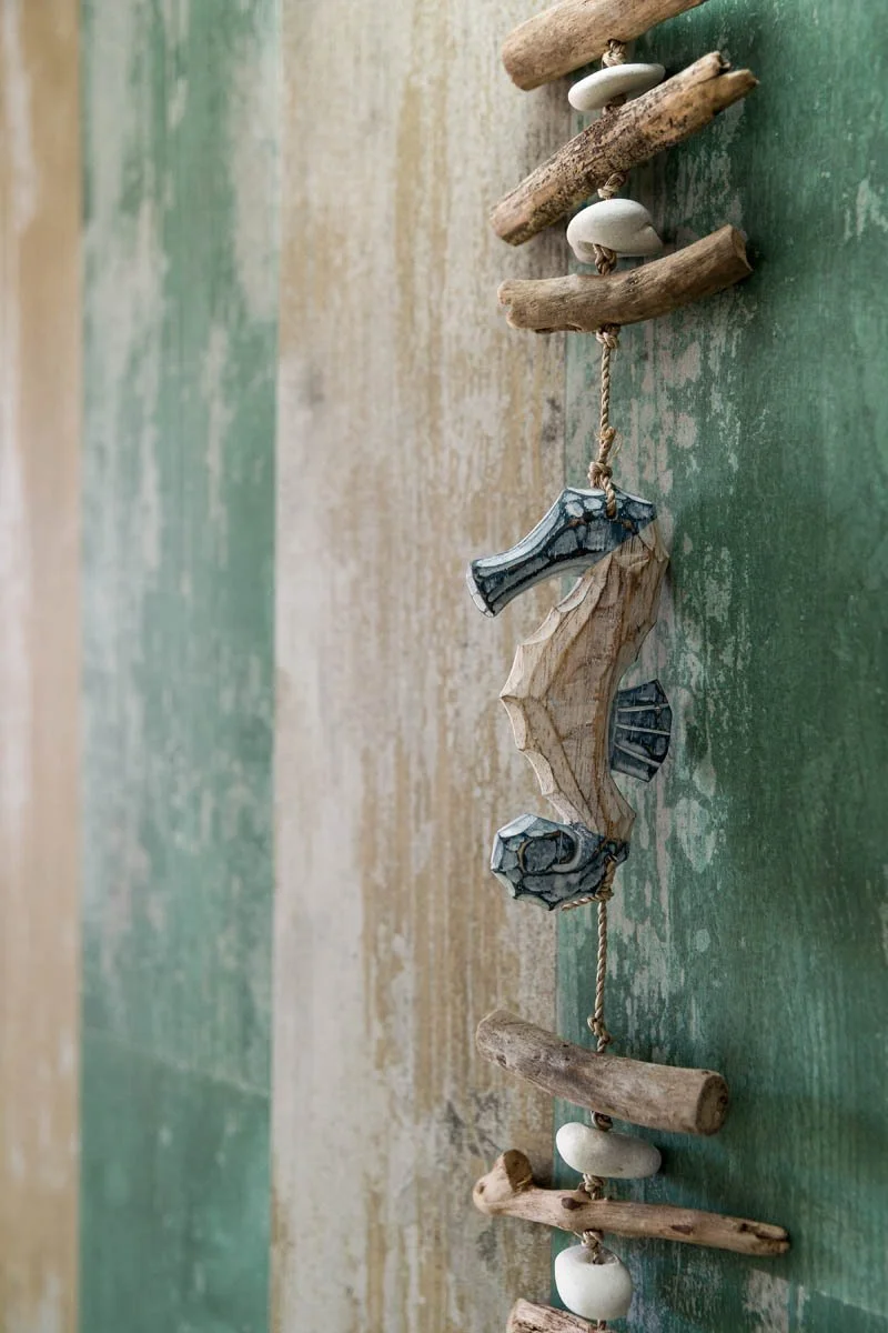 Decorativo com pedaços de madeira, pedras e corda, disposto sobre uma superfície de cor verde