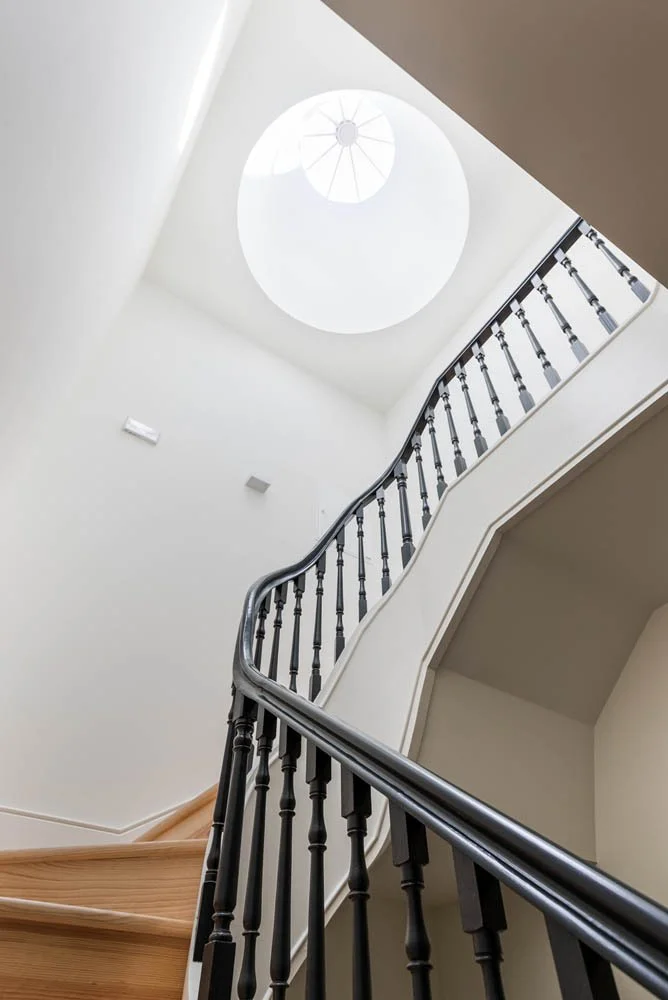 Escada interna de madeira com corrimão preto e rosetas decorativas na parede branca, vista de baixo.