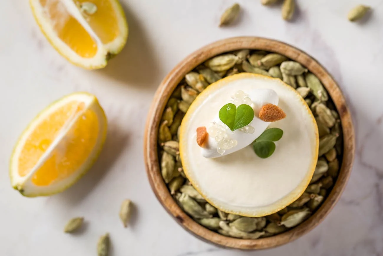 Pedaço de limão com creme, sementes de abóbora e gotas de essência decorando uma tigela de sementes de abóbora, com fatias de limão ao lado.
