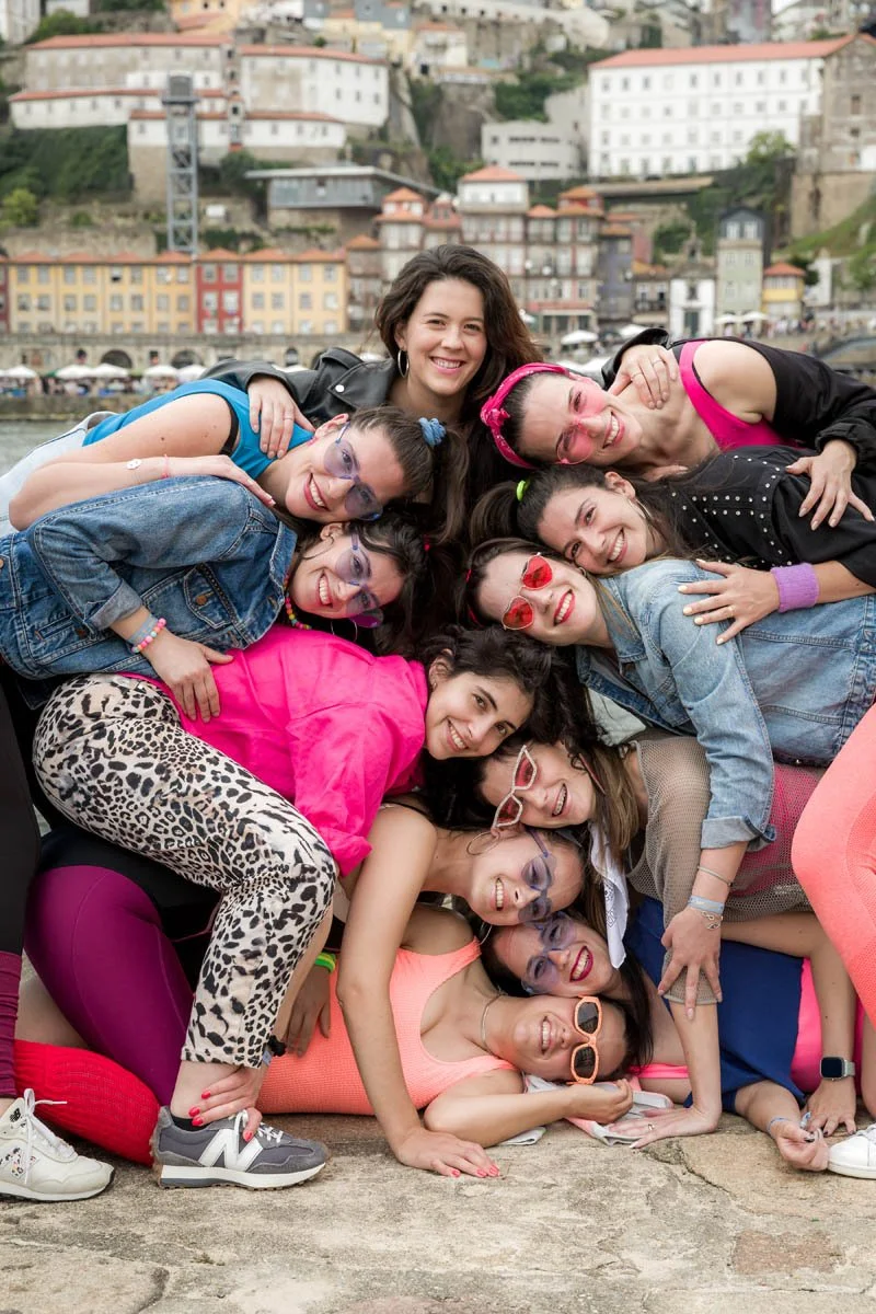 Grupo de pessoas sorridentes, com roupas coloridas, posando juntas ao ar livre com uma cidade de fundo.