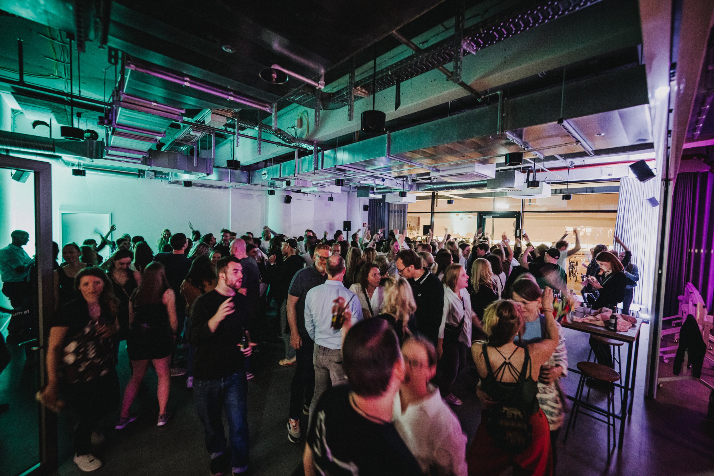 Menschen tanzen und feiern in einem Club mit bunten Lichtern und moderner Dekoration.