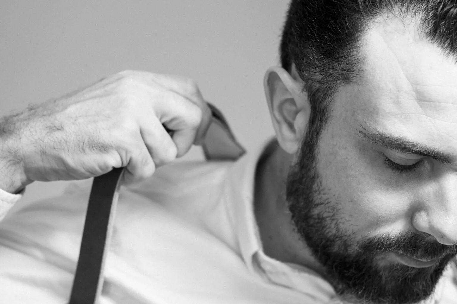 Black and white photograph of a bearded man adjusting his camera strap.