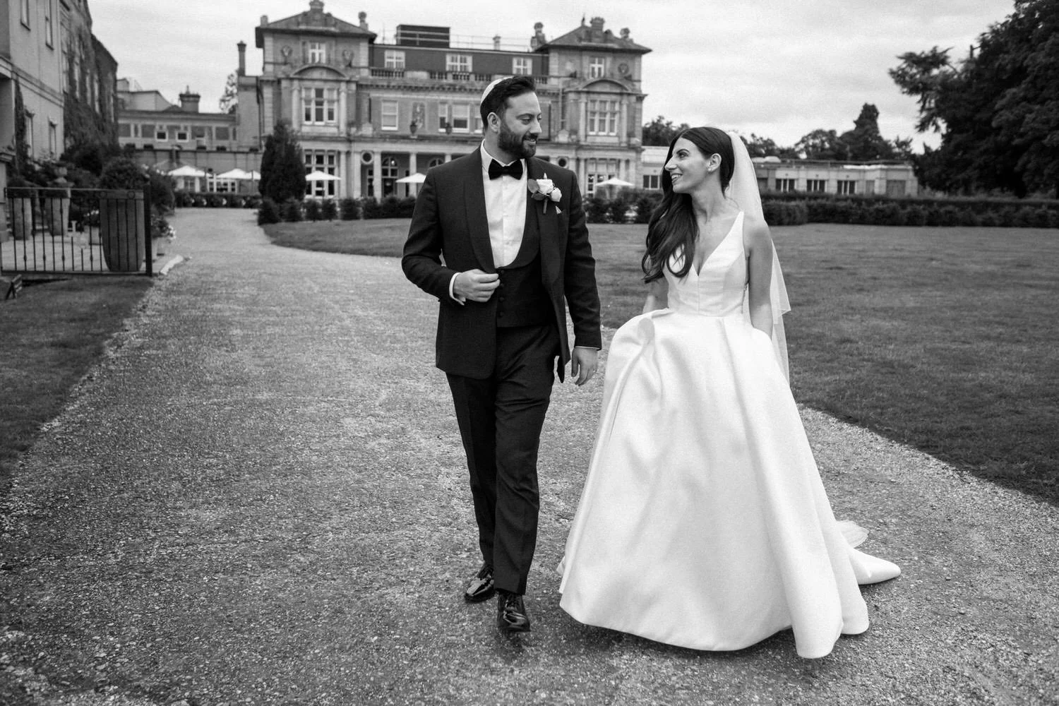 A documentary wedding photograph of a bride and groom smile on their wedding day as they walk the grounds of their Jewish wedding in Kent