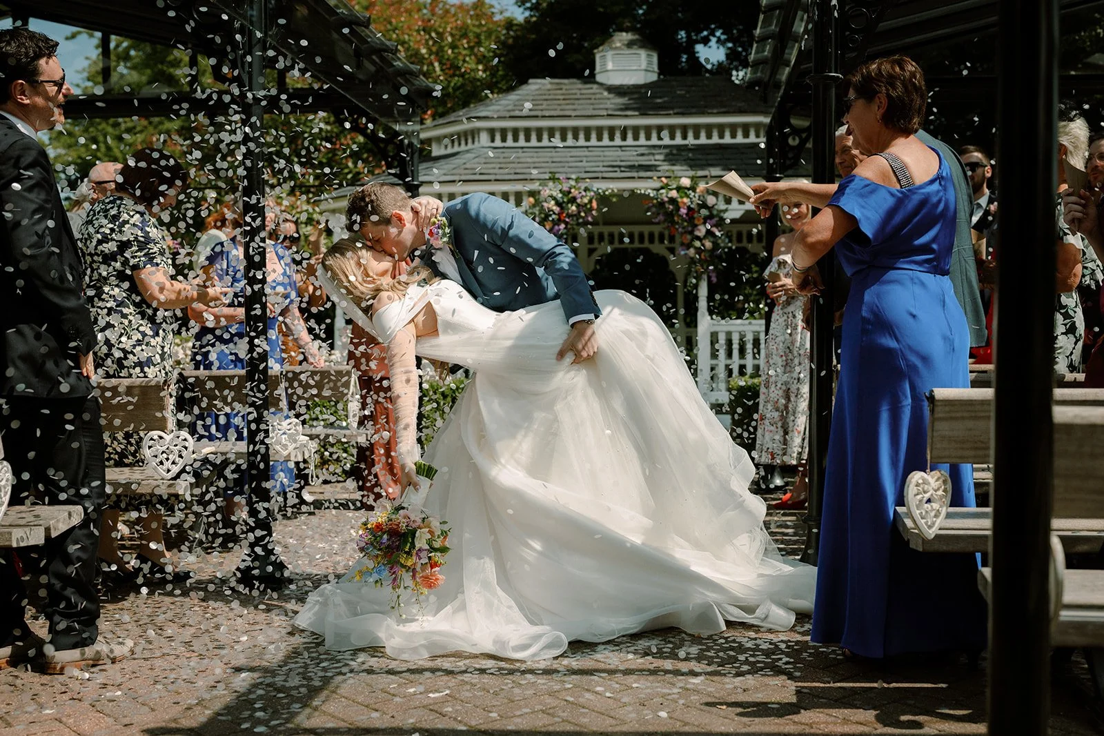 A husband dips his bride for a kiss while guests throw confetti at their wedding at The Old Kent Barn, Dover