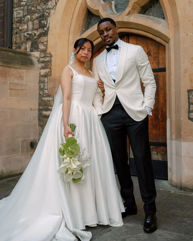 A documentary photograph of a fashionable mixed-race bride and groom editorialy poseed in front of a church in Kent