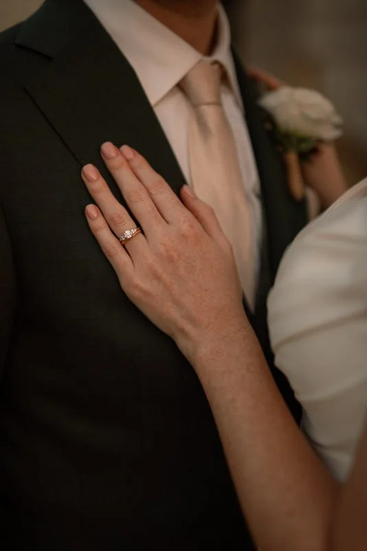 A documentary wedding photograph of a bride showing off her wedding ring on her husbands chest on their wedding day at golden hour in Hatfield Place in Kent