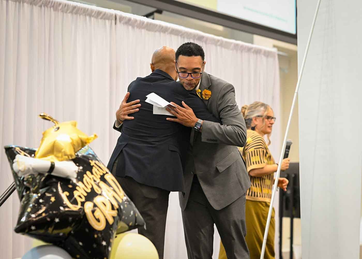 An African-American GYO-IL staff member and candidate hug on the graduation stage.