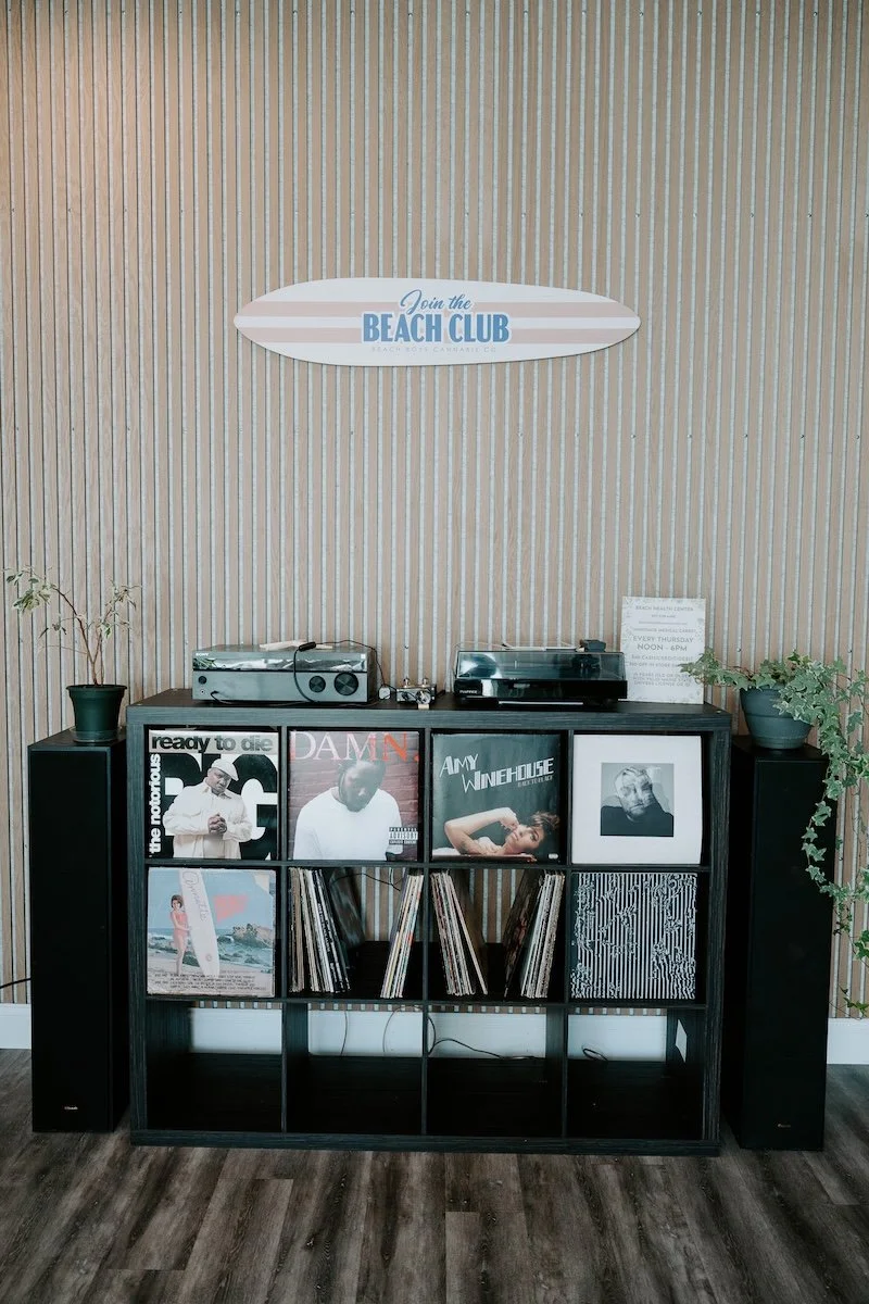 Vintage record player, vinyl collection, wood slat accent wall, and Beach Club surfboard display inside Beach Boys Cannabis Co.'s South Portland recreational weed shop. The Beach Club blends Maine's coastal lifestyle with a modern retail experience f