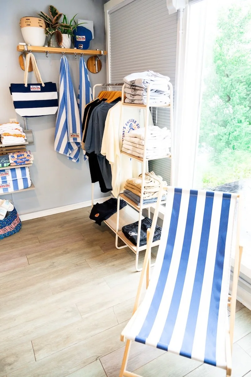 Beach Club apparel and merchandise display inside Beach Boys Beach Club in Old Orchard Beach, Maine. Shop exclusive t-shirts, hoodies, hats, and accessories while visiting our 21+ recreational cannabis dispensary just steps from the beach.