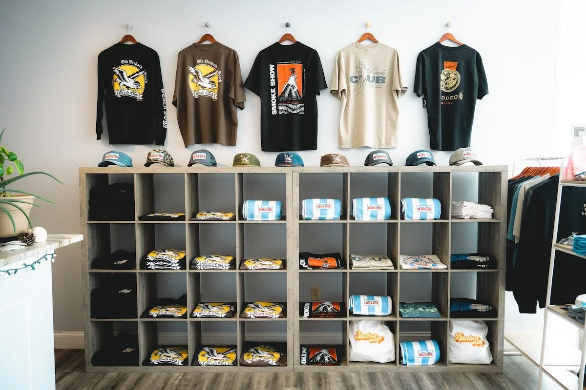 Beach Club apparel and merchandise display inside Beach Boys Cannabis Co.'s 21+ recreational weed shop in South Portland, Maine. Shop exclusive hats, t-shirts, hoodies, and accessories while visiting our adult-use cannabis dispensary just minutes fro